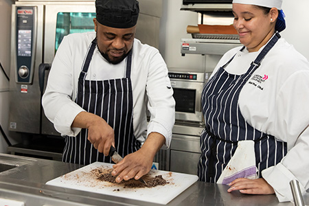 A student working with the chef in the kitchen